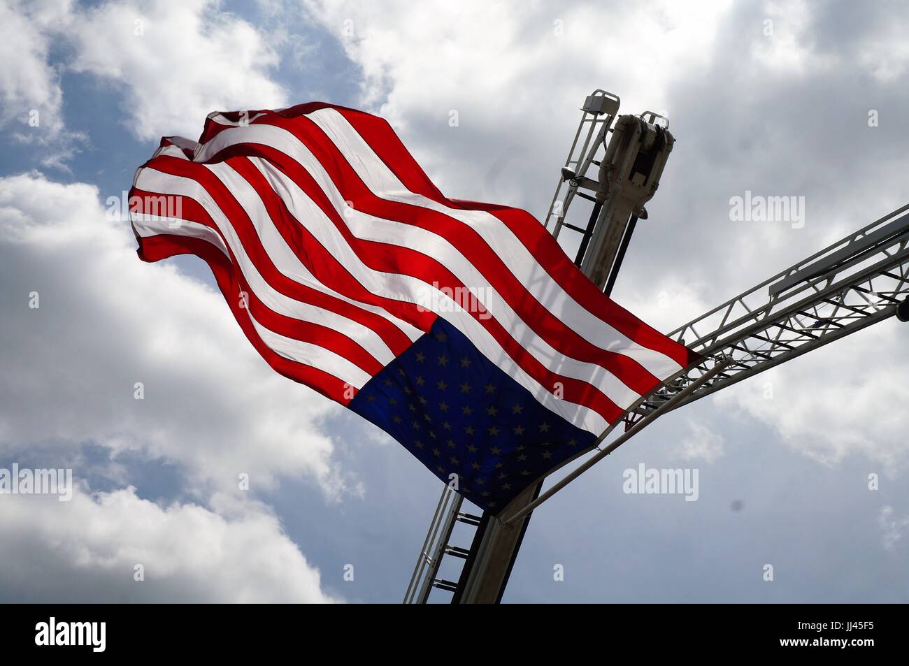 American flag suspended from fire trucks waving in blue sky Stock Photo
