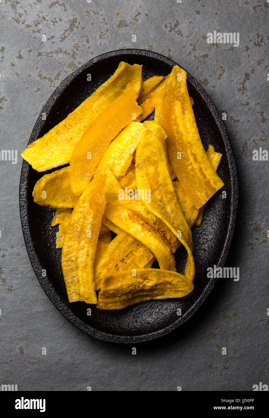 Healthy Homemade banana Plantain Chips on black plate, slate background