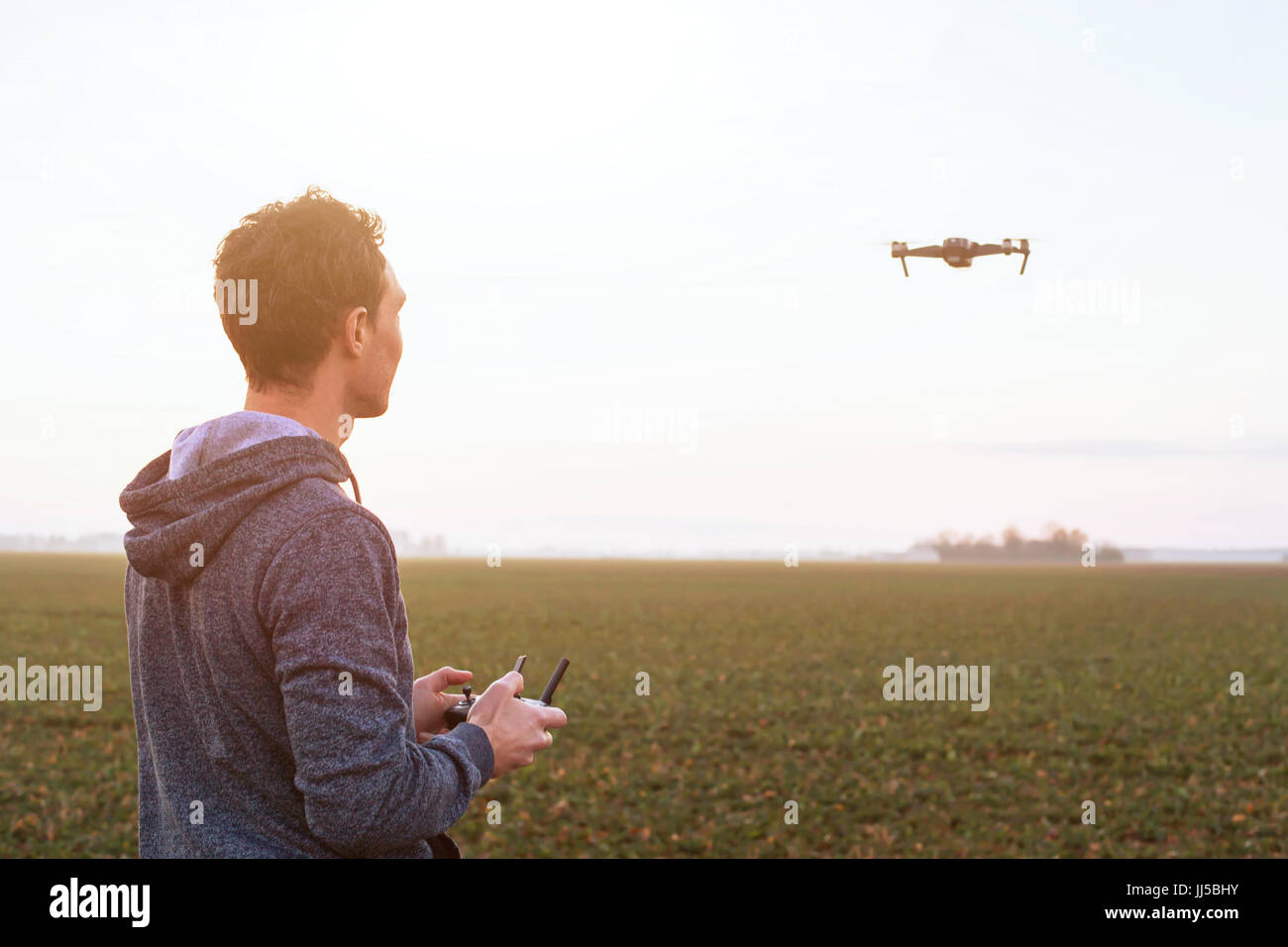 man piloting drone at sunset field, uav technology background Stock Photo