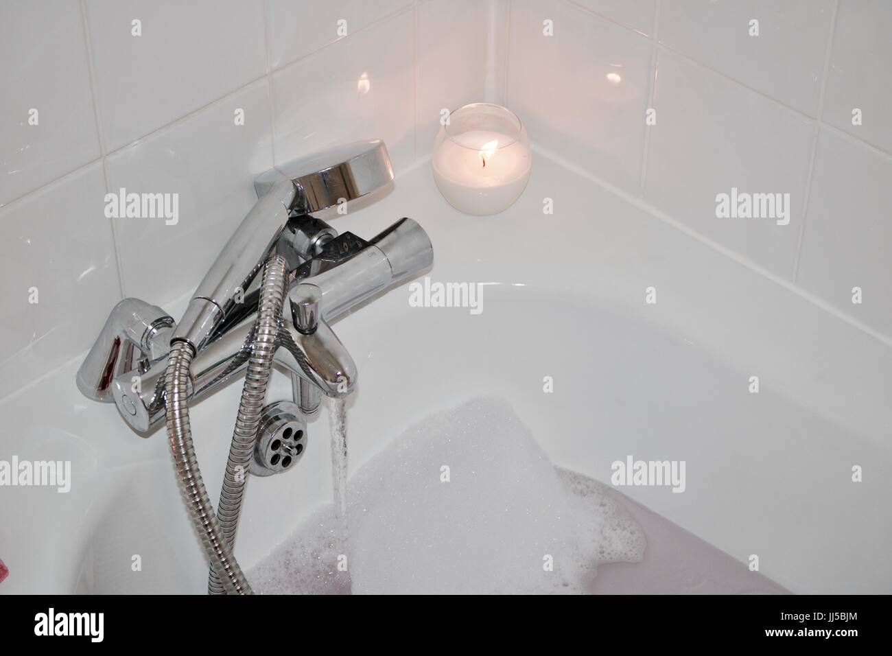 White candle in bathroom near hot water and foam. Bath concept Stock