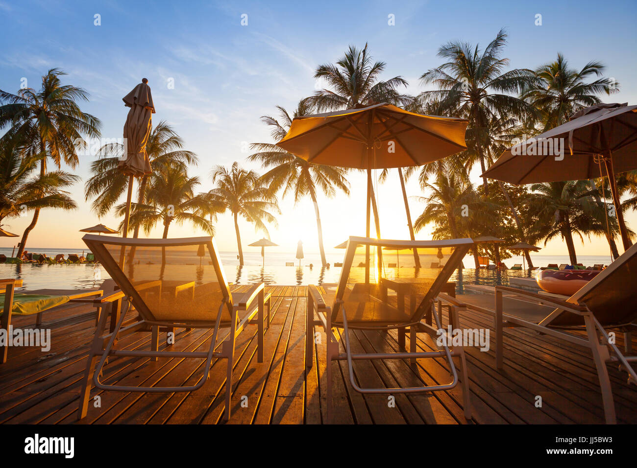 two deckchairs near swimming pool at sunset in luxury beach hotel on tropical island Stock Photo