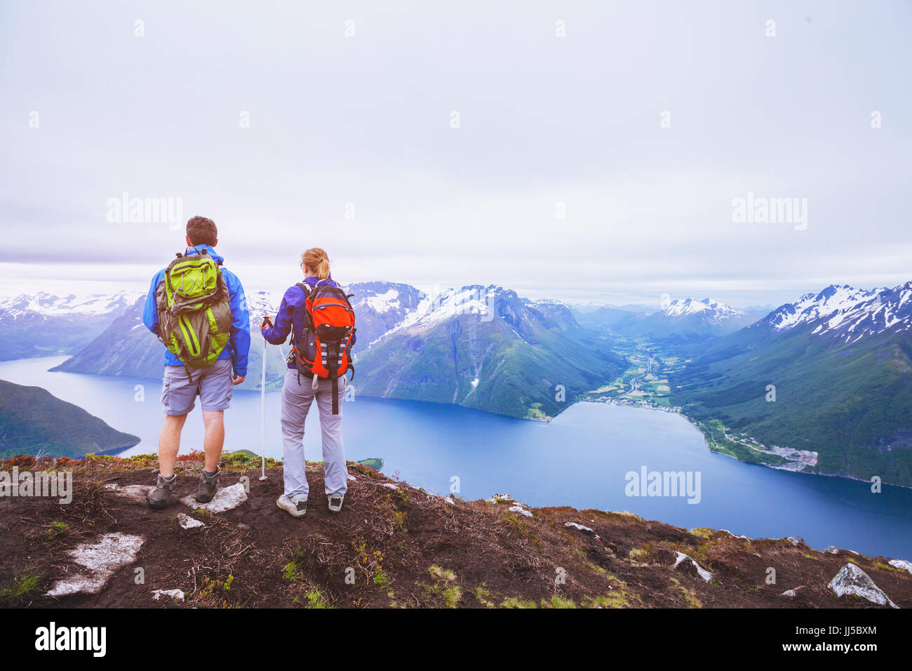 couple of hikers on top of the mountain, group of backpackers traveling in Norway fjords, people looking at beautiful panoramic landscape Stock Photo