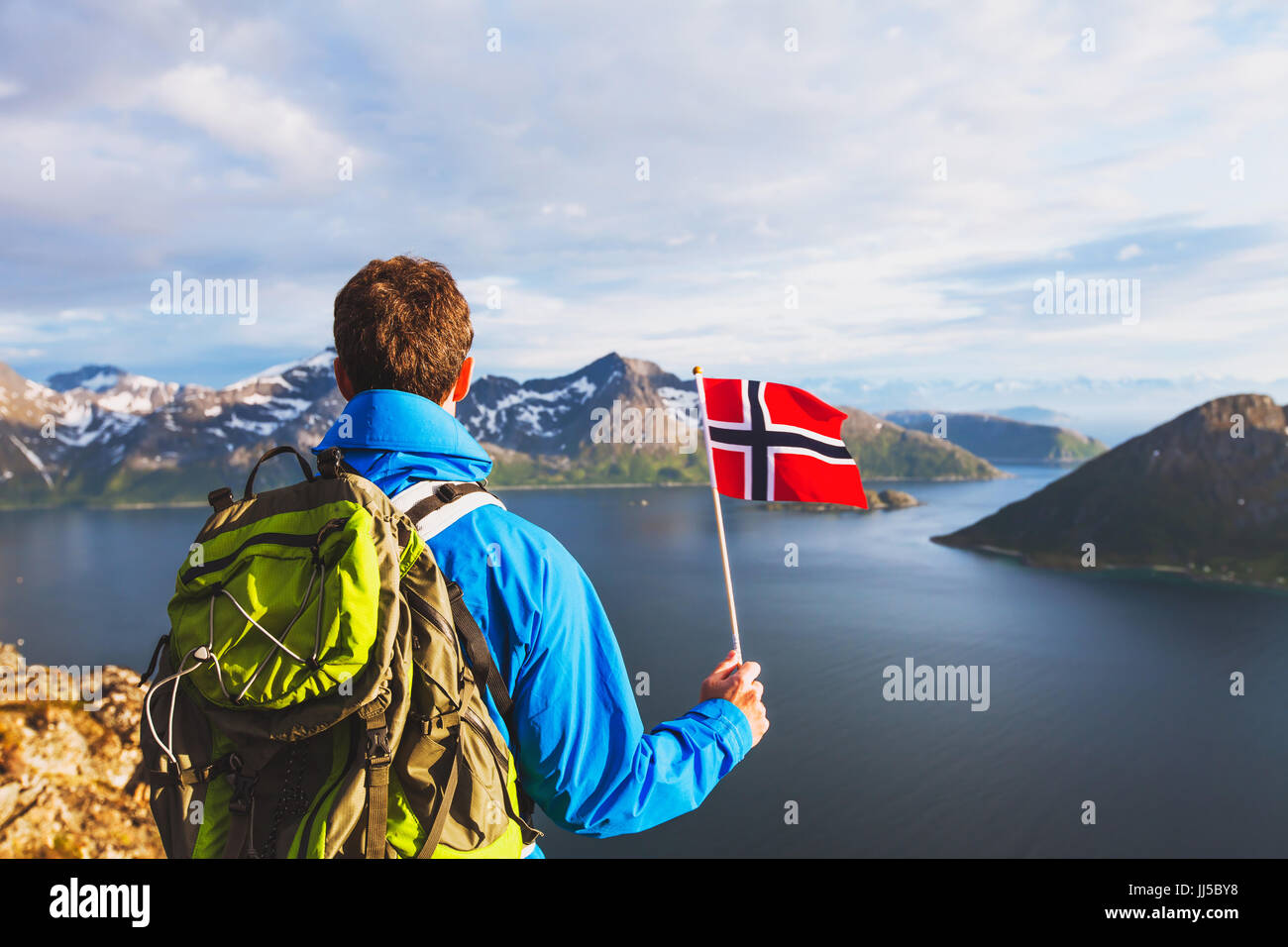 travel to Norway, hiker traveler with backpack holding norwegian flag and looking at beautiful fjord landscape Stock Photo