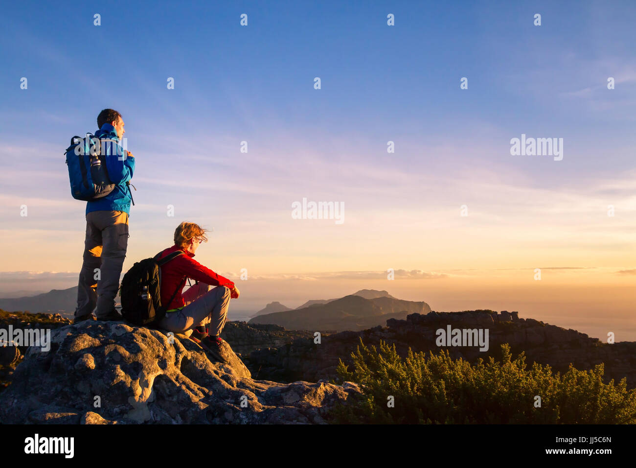 couple of hikers with backpacks enjoying panoramic view of sunset in mountains, travel and outdoor adventure concept Stock Photo