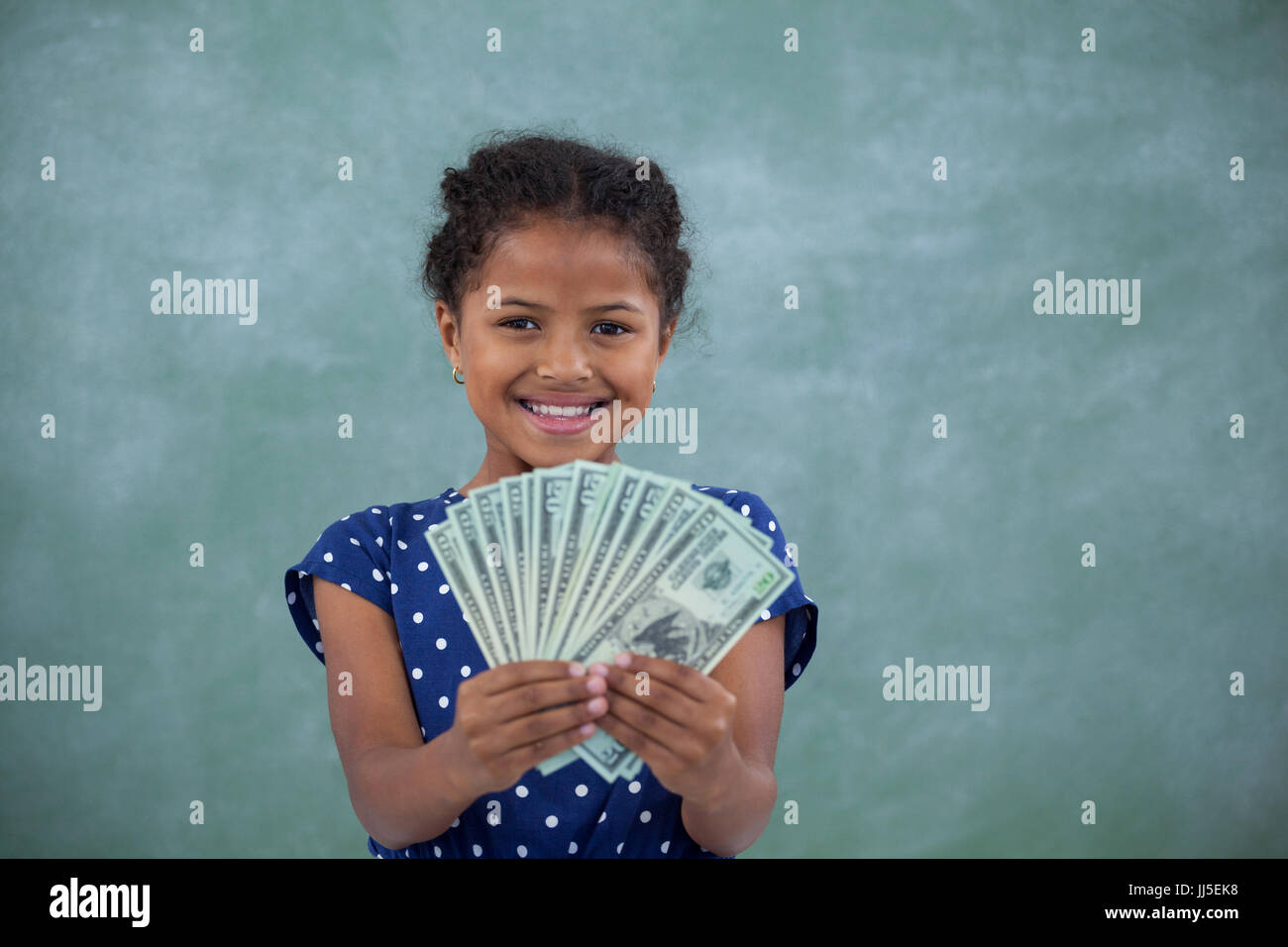 Happy girl showing paper currency while standing against wall Stock Photo