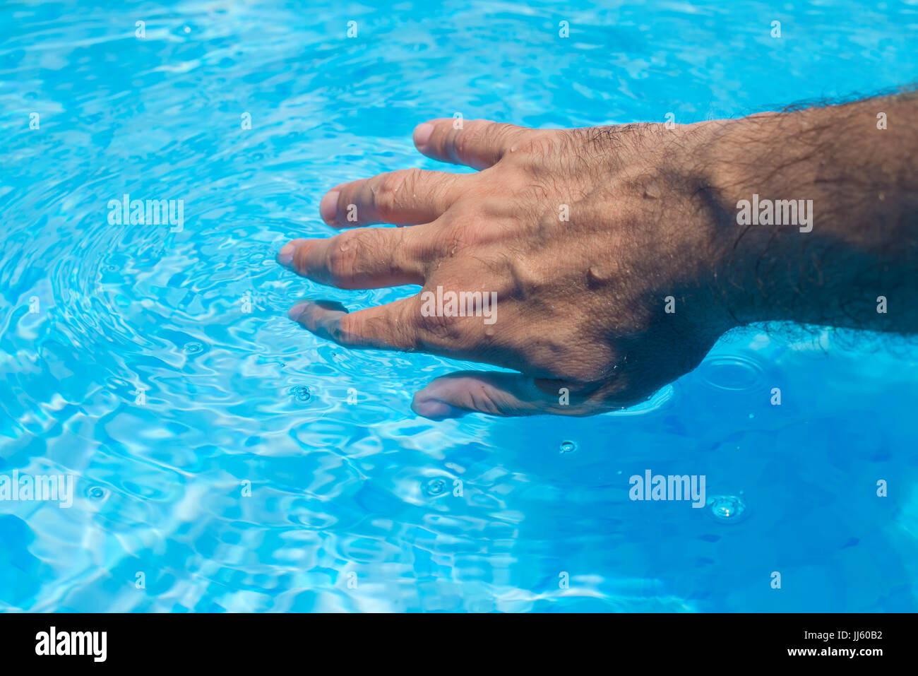 Male hand touching clear swimming pool water, summer activity by the poolside Stock Photo