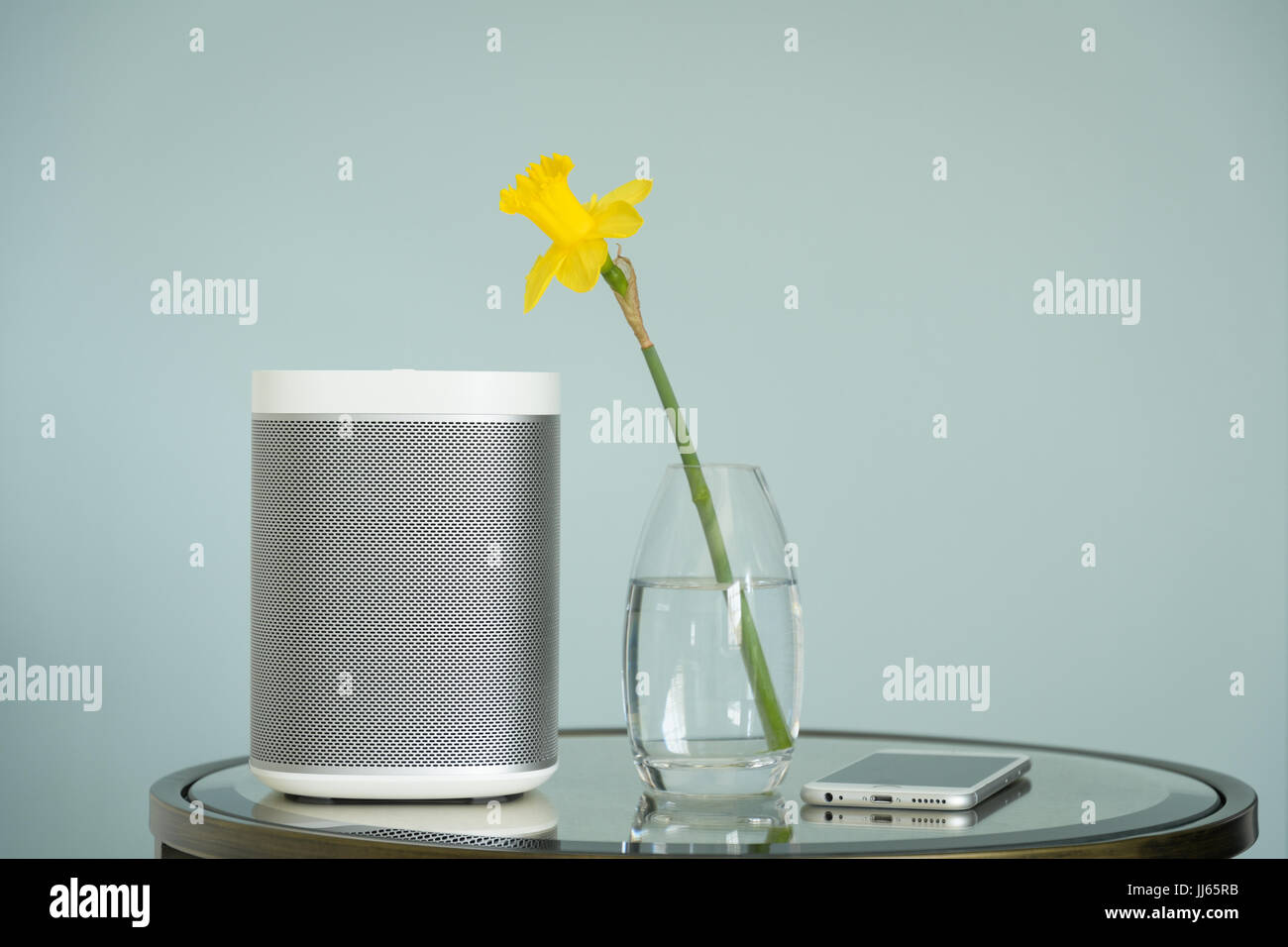 Wireless speaker and mobile phone on a mirrored table with a yellow daffodil. Stock Photo