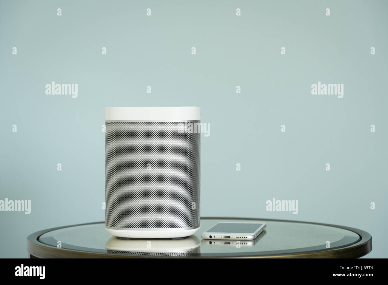 Wireless speaker on a mirrored table and a mobile phone against a light blue background. Stock Photo