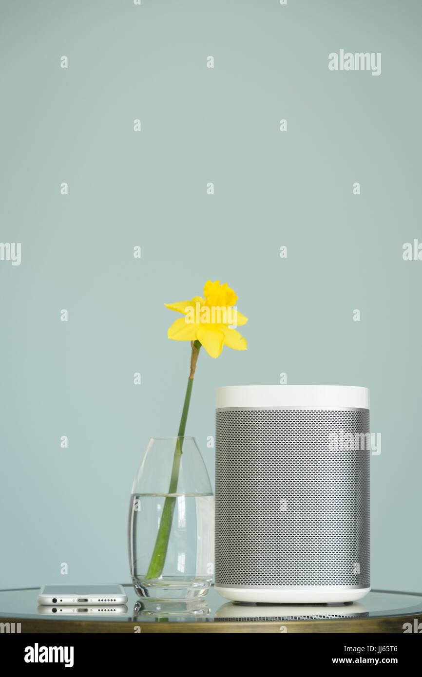 Wireless speaker and mobile phone on a mirrored table with a yellow daffodil. Stock Photo