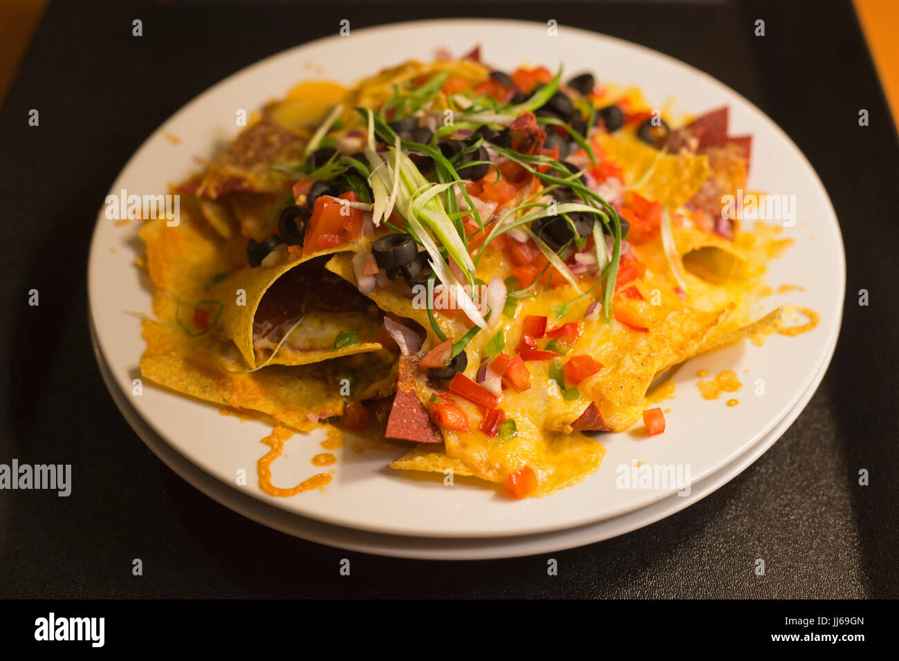 Plate of nachos with melted cheese, black olives, green onions, red peppers, green peppers and tomatoes on room service tray Stock Photo