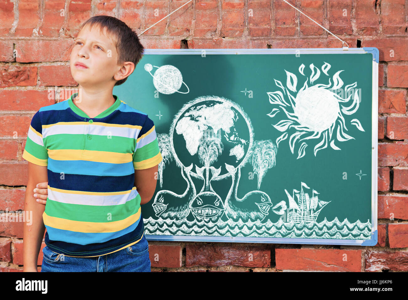 Meditative boy near chalkboard with drawing Earth map on three whales in the improvised outdoor class Stock Photo