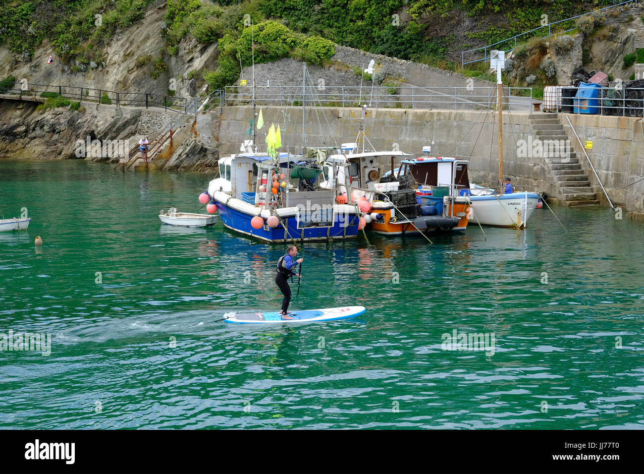 Man paddleboarding passed small fishing boats in Newquay Harbour Stock Photo