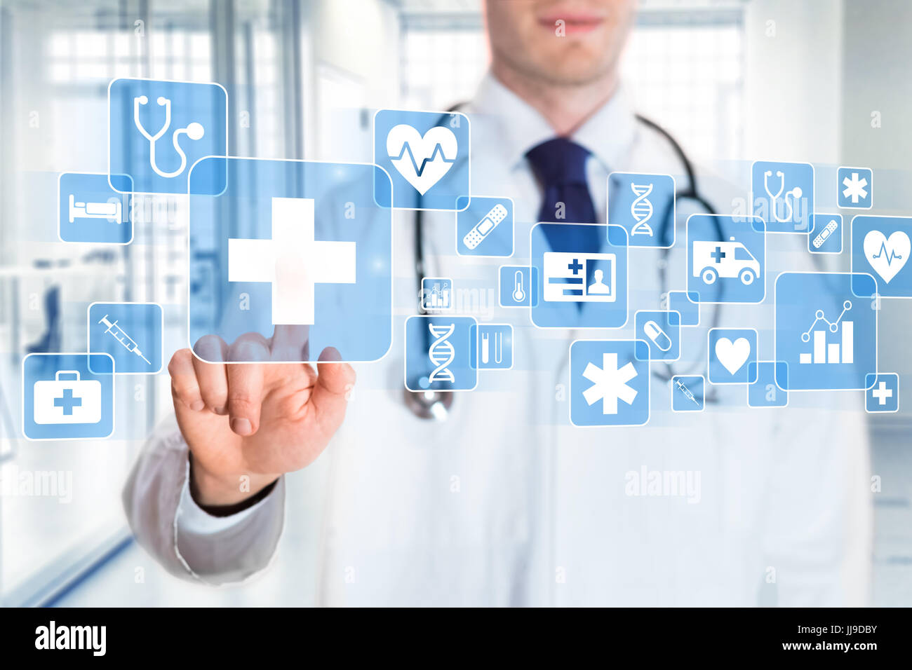 Medical doctor showing icons of health care services (cross, heart, DNA, insurance card, ambulance symbols) on a digital screen with hospital interior Stock Photo