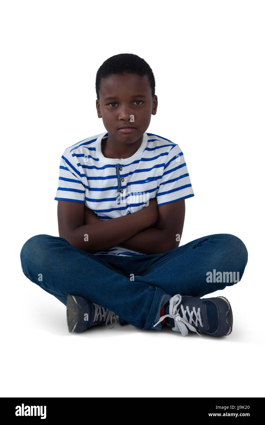 Portrait of sad boy sitting on floor against white background Stock Photo