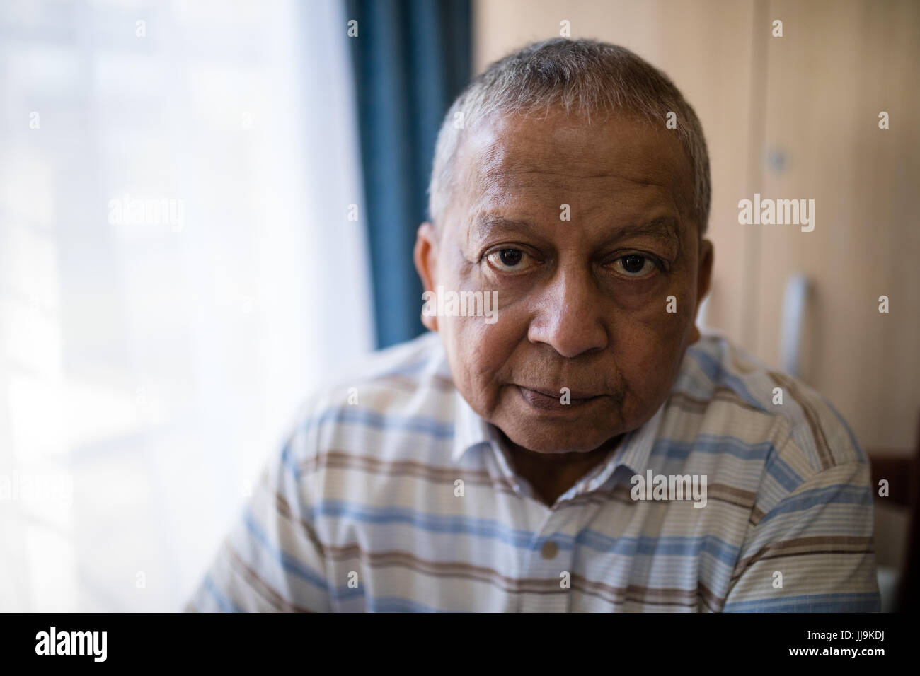 Portrait of serious senior man by window at nursing home Stock Photo