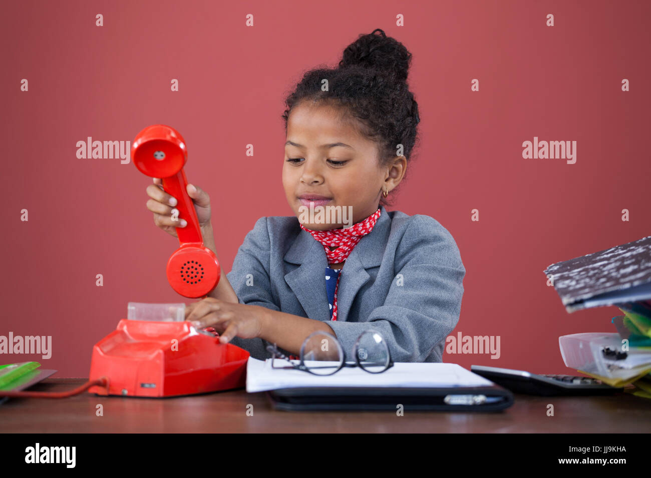 Businesswoman using land line phone while working at desk against orange background Stock Photo