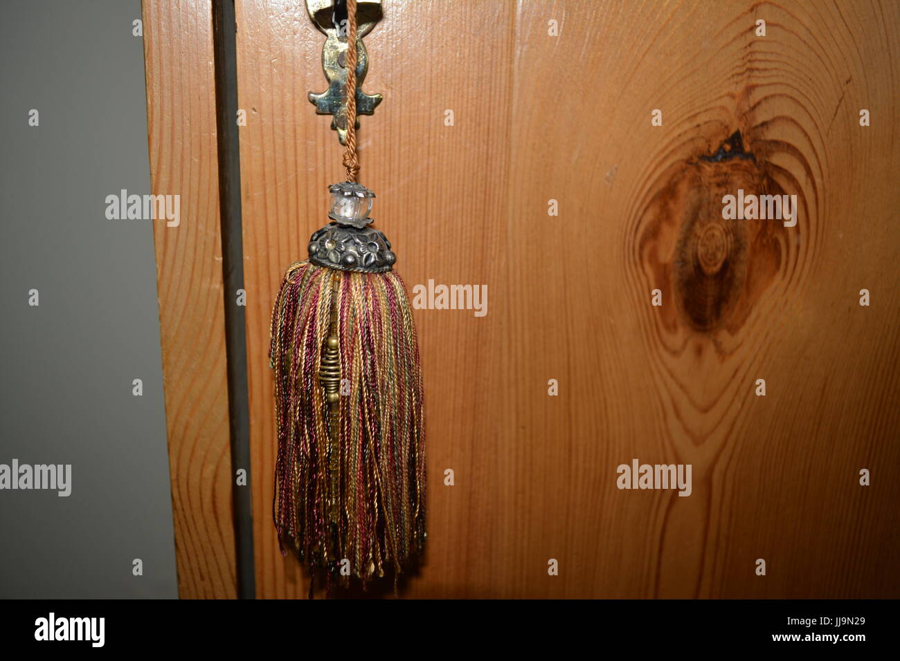 Decorative multi colour color colourful tassel tassle decoration hanging from key in brass lock to antique pine lockable cupboard cabinet Stock Photo