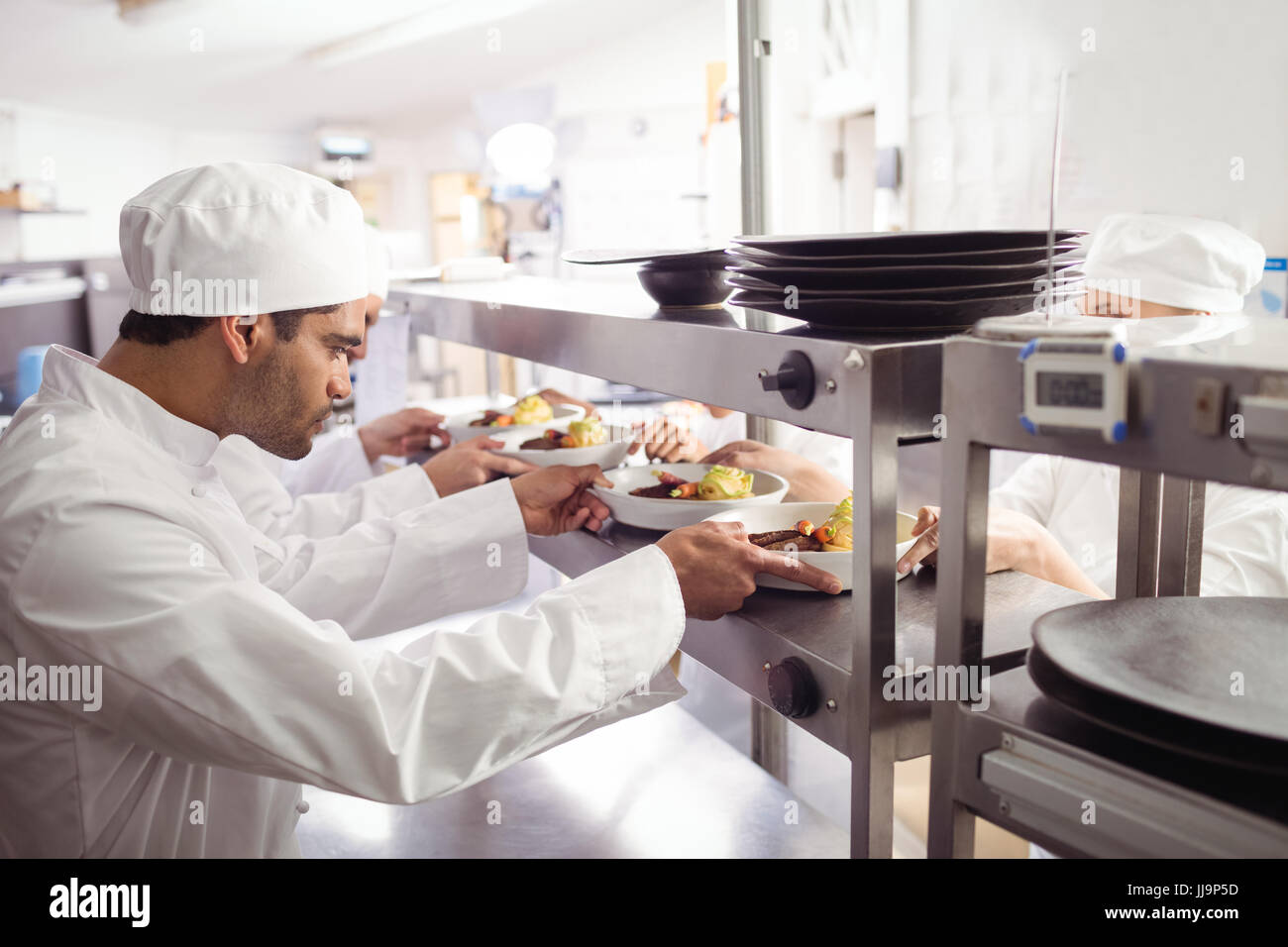 Chefs passing ready food to waiter at order station in commercial