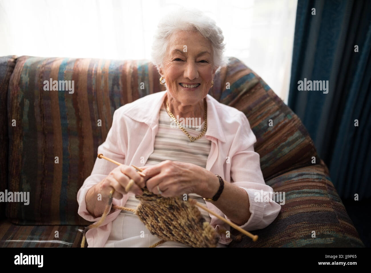 Portrait of smiling senior woman knitting while sitting on sofa against ...