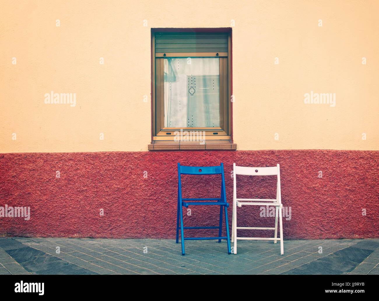 cross-processed image of two wooden chairs below window at house wall in countryside in Spain Stock Photo