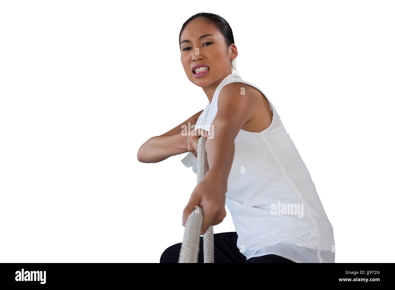 Portrait of woman clenching teeth while pulling rope against white