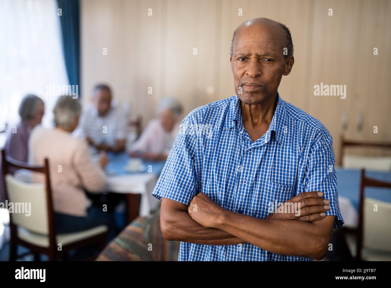 Portrait of senior man standing with arms crossed against friends at ...