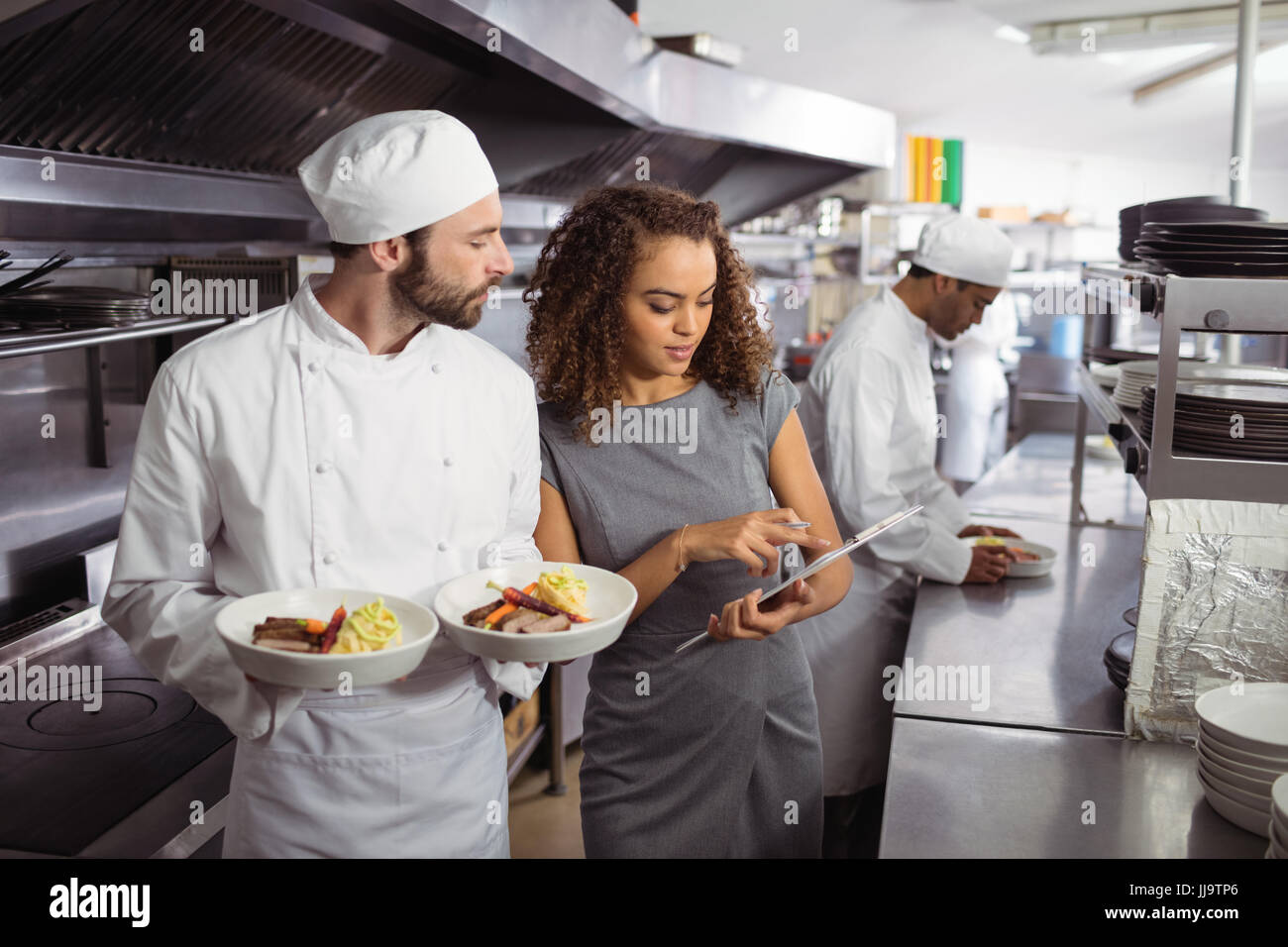 Chefs discussing menu on clipboard in commercial kitchen Stock Photo ...