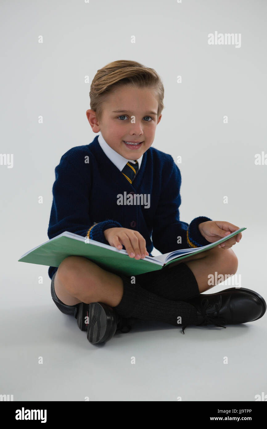 Portrait of schoolboy reading book while sitting on white background ...