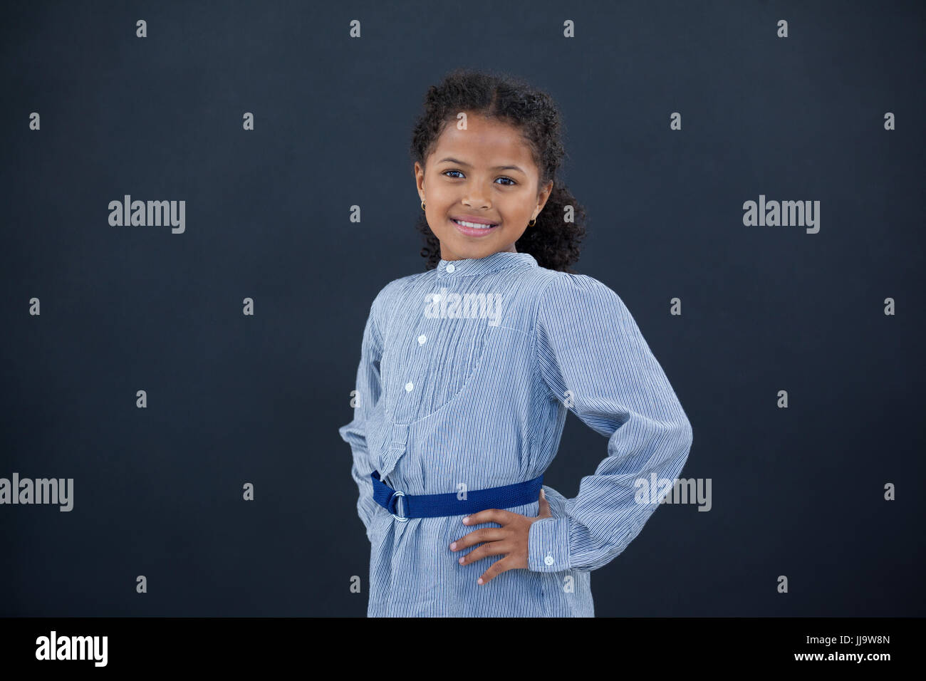 Portrait of happy girl with hand on hip standing against black ...