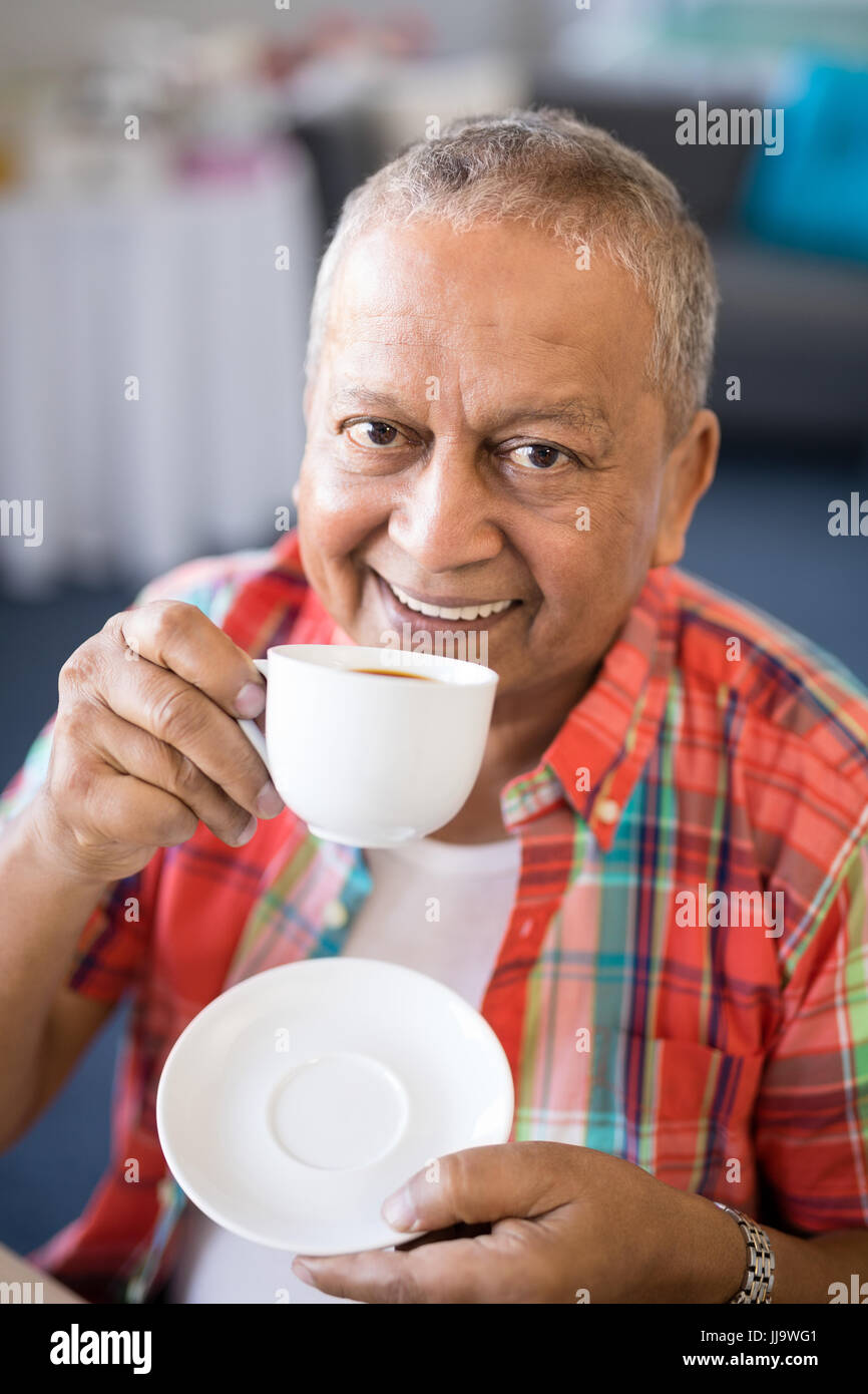 Portrait of smiling senior man drinking coffee while sitting in nursing