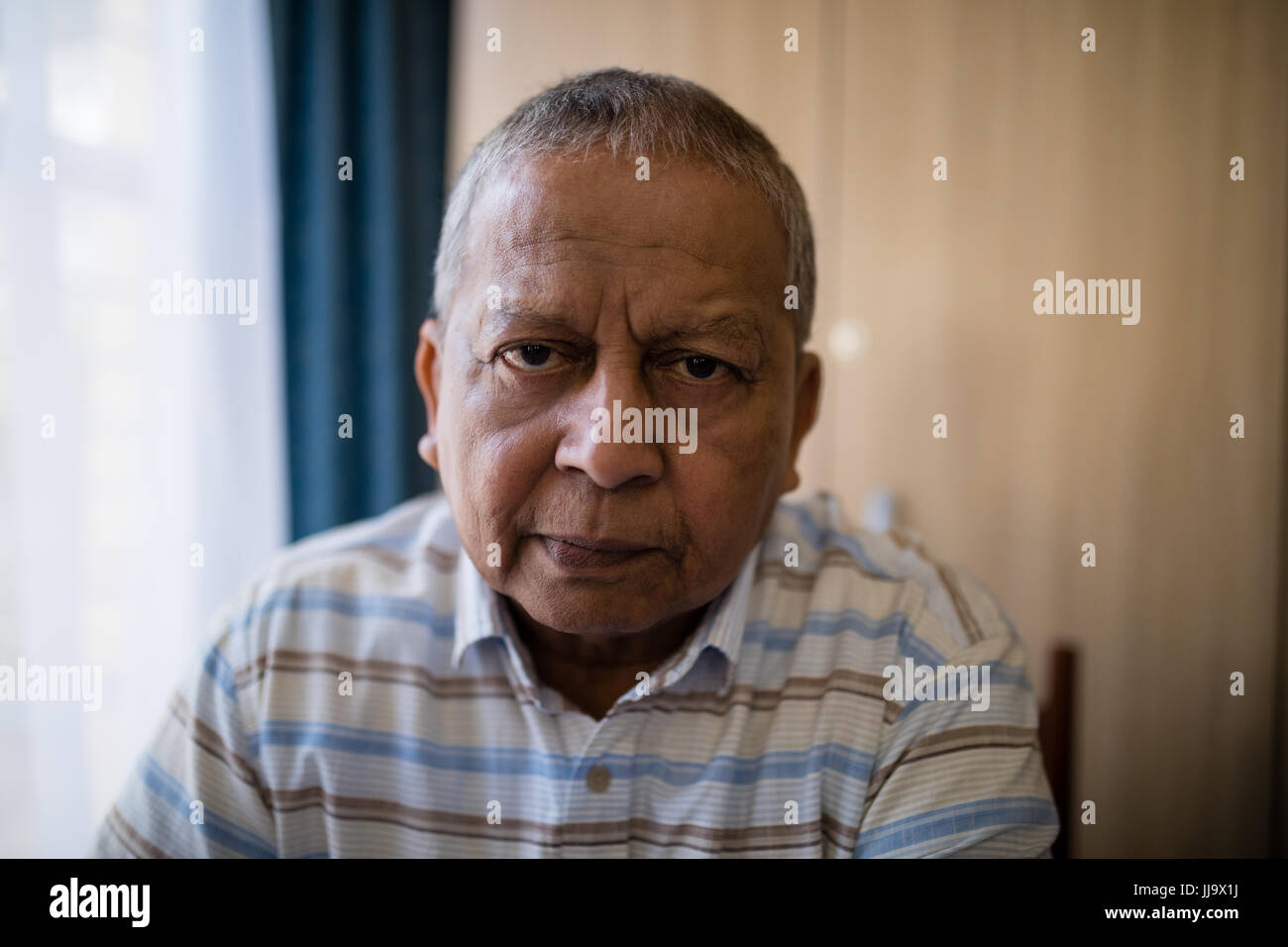 Portrait of senior man sitting by window at nursing home Stock Photo
