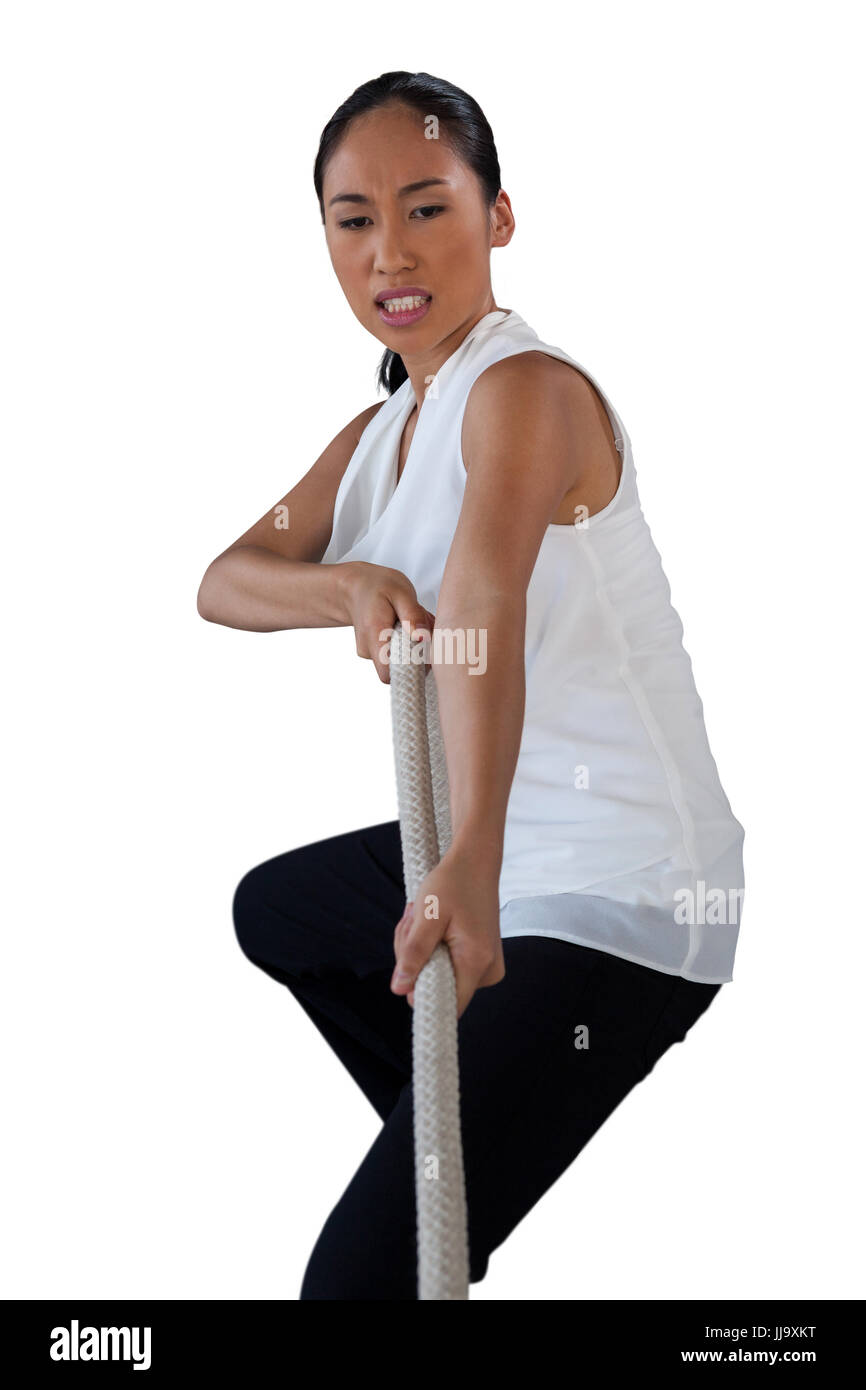 Young woman clenching teeth while pulling rope against white background