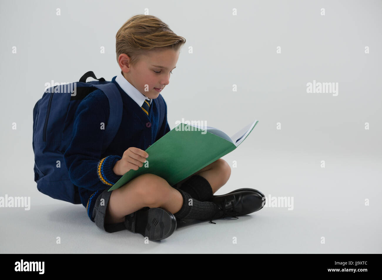 Adorable schoolboy reading book while sitting on white background Stock ...