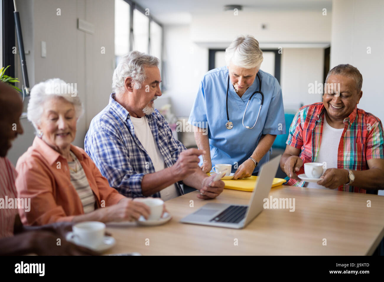 Healthcare worker serving coffee to senior people using laptop while ...