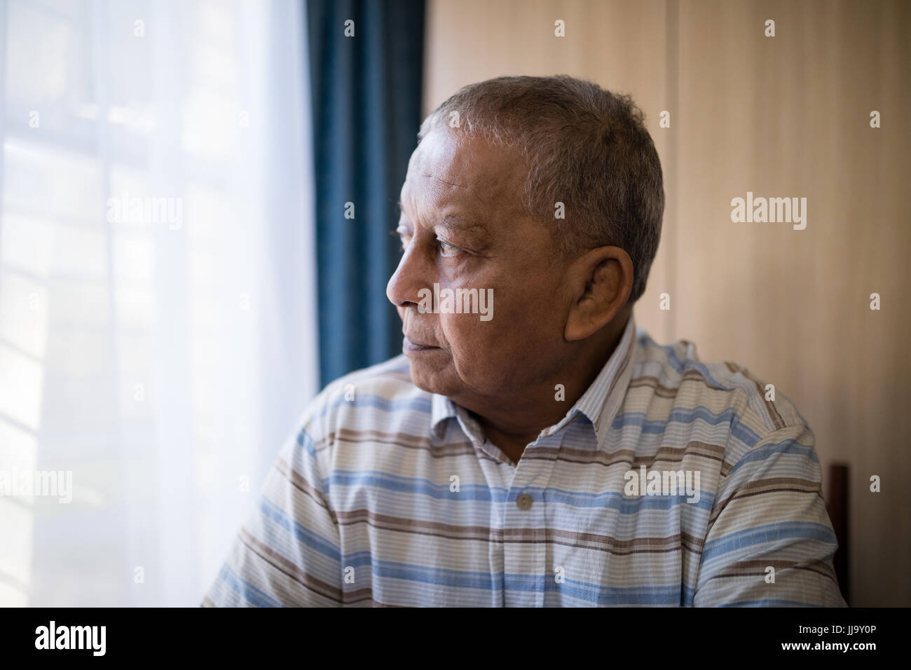 Thoughtful senior man by window at nursing home Stock Photo