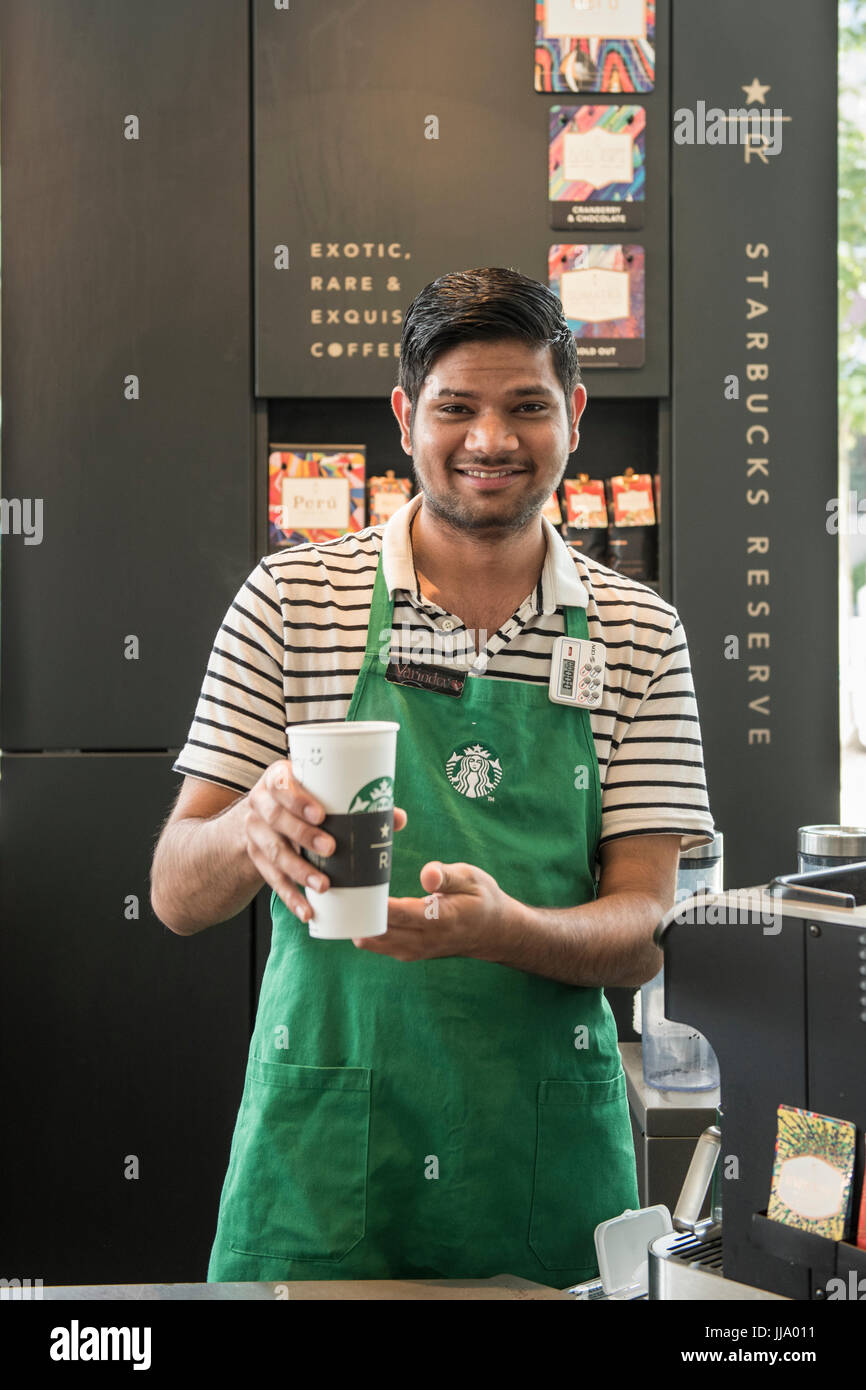 Starbucks Barista looking at the camera smiling, holding up a cup