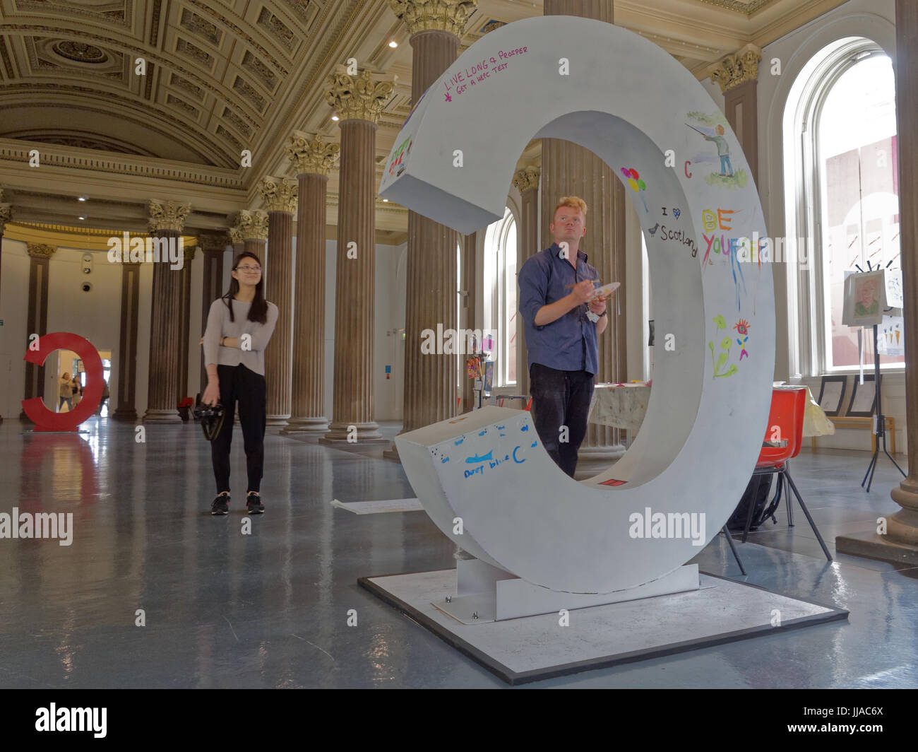 Glasgow, Scotland, UK. 18th July, 2017. National Exhibition for World Hepatitis Day at the Gallery of Modern Art  organized by Hepatitis See Community Art and Digital Photography Project uses visual art to bring together and connect people living with hepatitis C. John Martin decorates a C and one of the charity's staff watches on. Credit Gerard Ferry/Alamy news Stock Photo