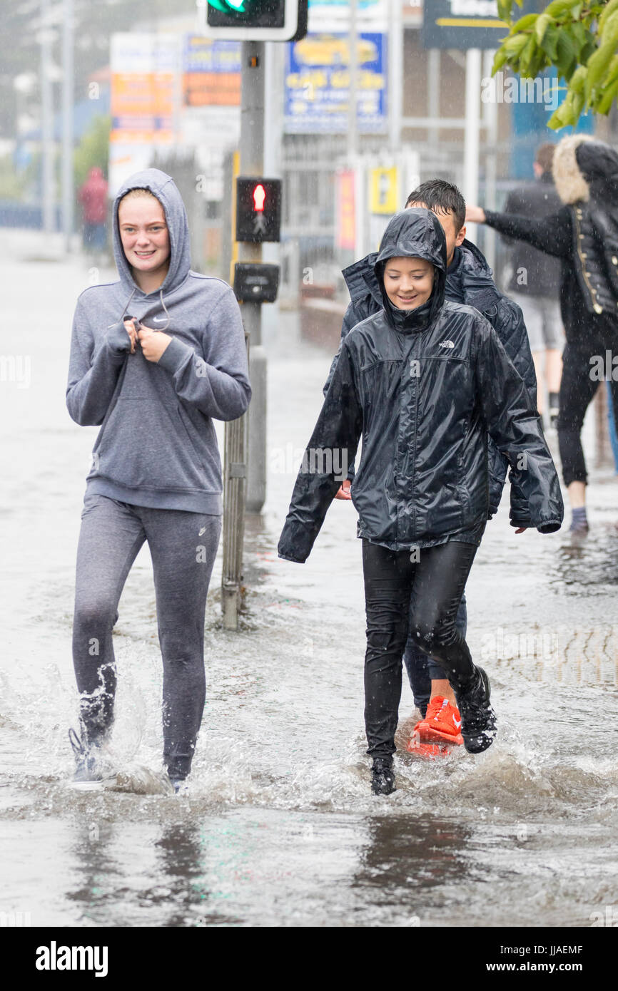 People caught out by torrential rain and flash flooding during a summer storm as they walk through flooded streets on the A525 road in the coastal resort town of Rhyl, Denbighshire, Wales, UK Stock Photo