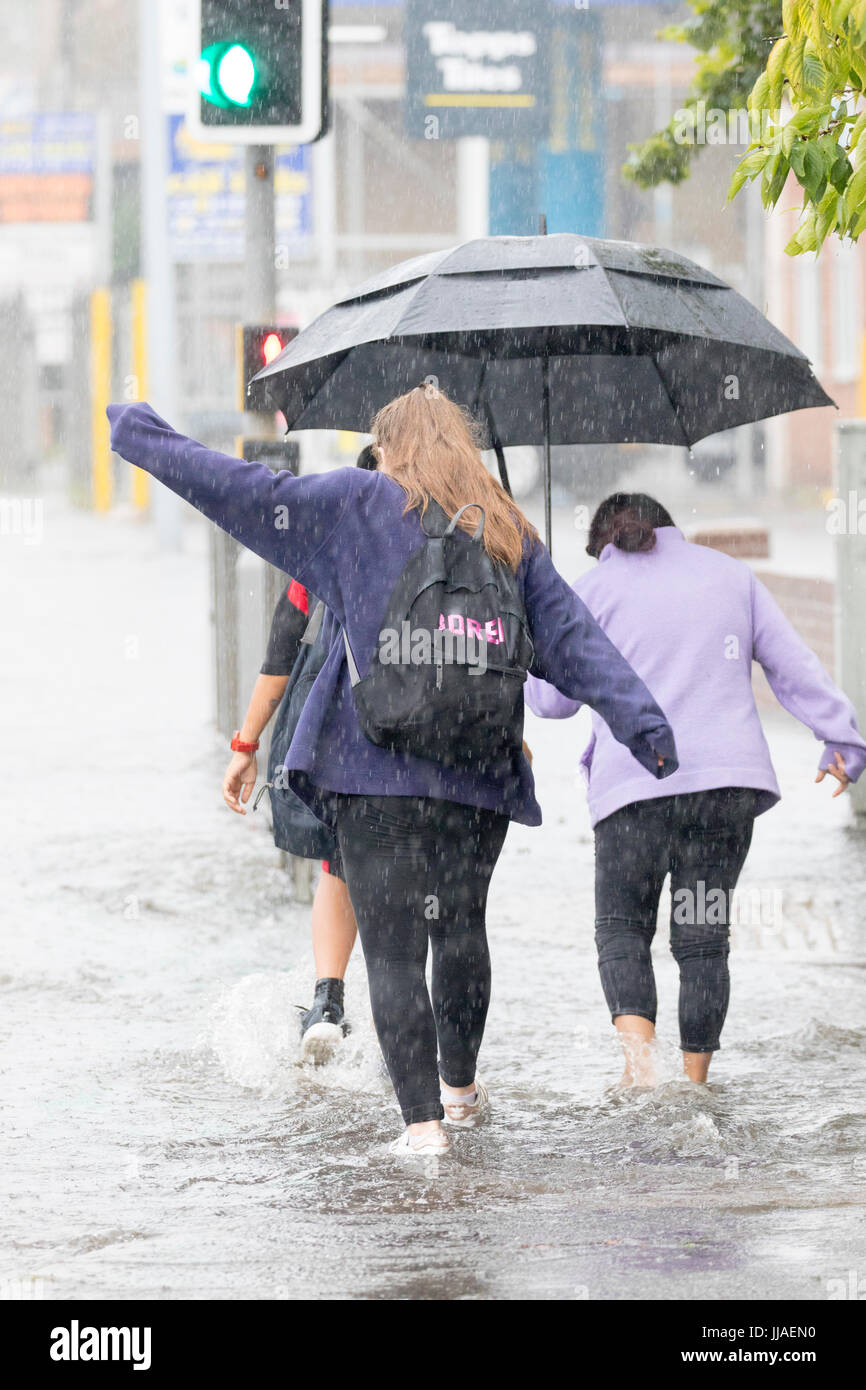 People caught out by torrential rain and flash flooding during a summer storm as they walk through flooded streets on the A525 road in the coastal resort town of Rhyl, Denbighshire, Wales, UK Stock Photo