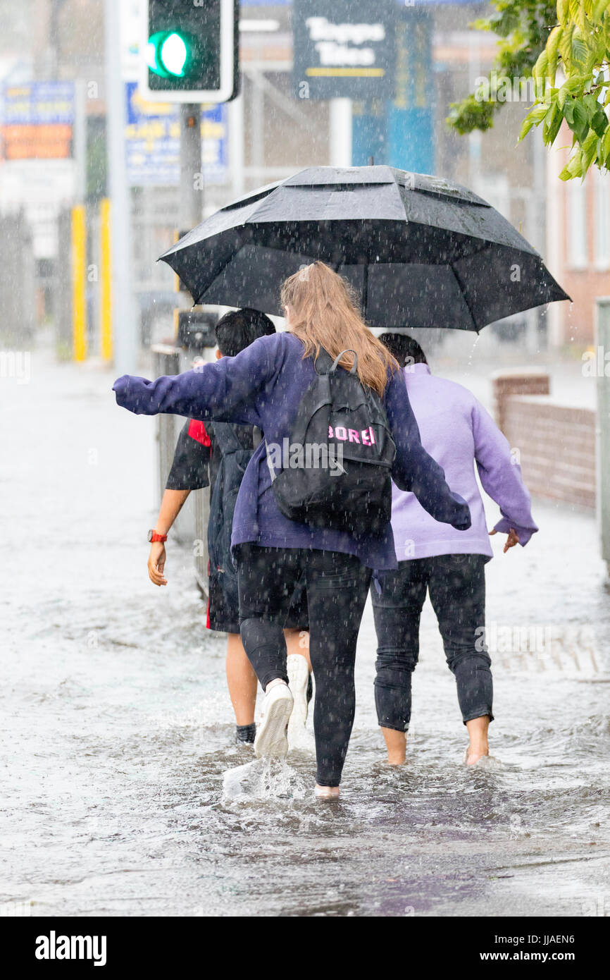 People caught out by torrential rain and flash flooding during a summer storm as they walk through flooded streets on the A525 road in the coastal resort town of Rhyl, Denbighshire, Wales, UK Stock Photo