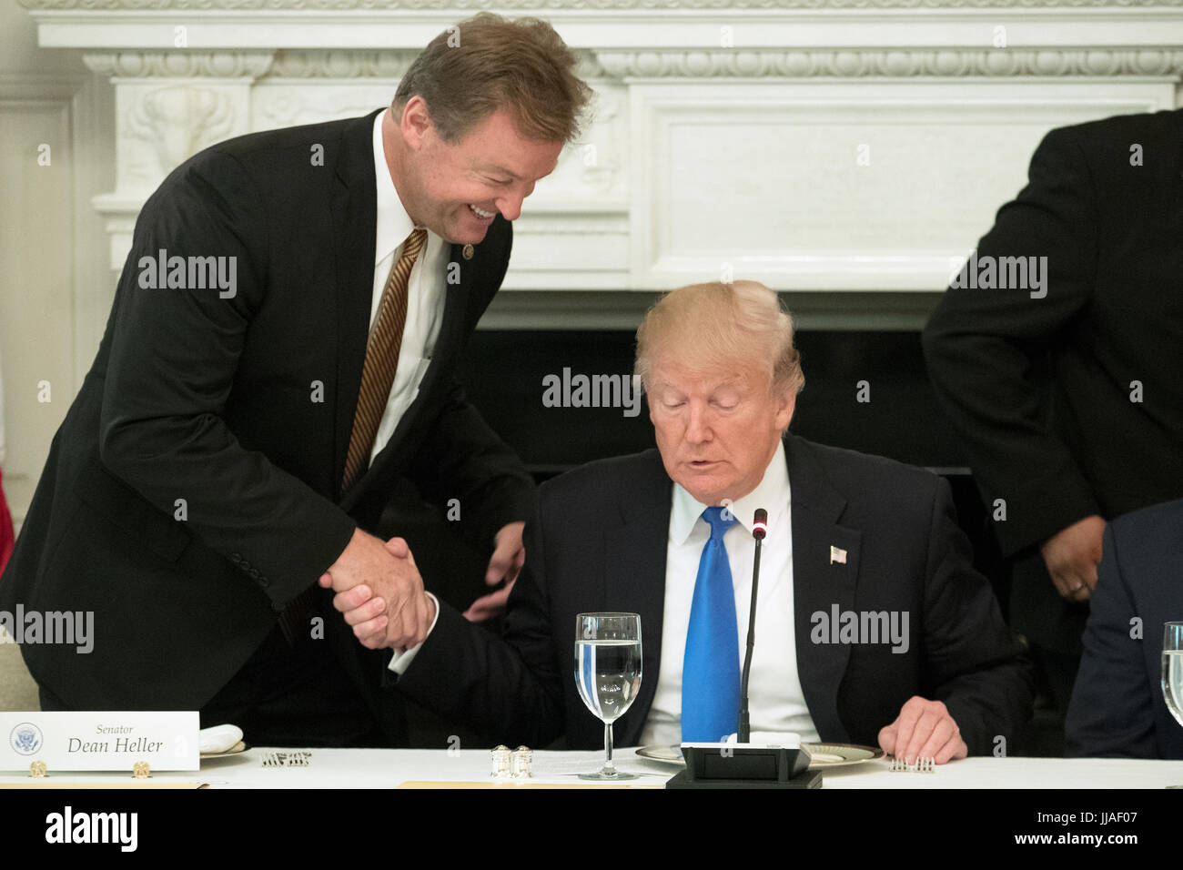 US President Donald J. Trump (R) shakes hands with Republican Senator from Nevada Dean Heller (L) after taking his seat to deliver remarks on health care and Republicans' inability thus far to replace or repeal the Affordable Care Act, during a lunch with members of Congress in the State Dining Room of the White House in Washington, DC, USA, 19 July 2017. Credit: Michael Reynolds/Pool via CNP /MediaPunch Stock Photo