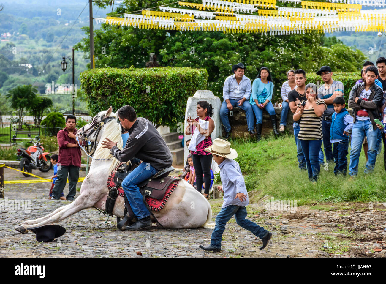 San Juan del Obispo, Guatemala - June 12, 2016: Cowboy makes horse lie down as part of show in horse street parade in village near Antigua, Guatemala Stock Photo