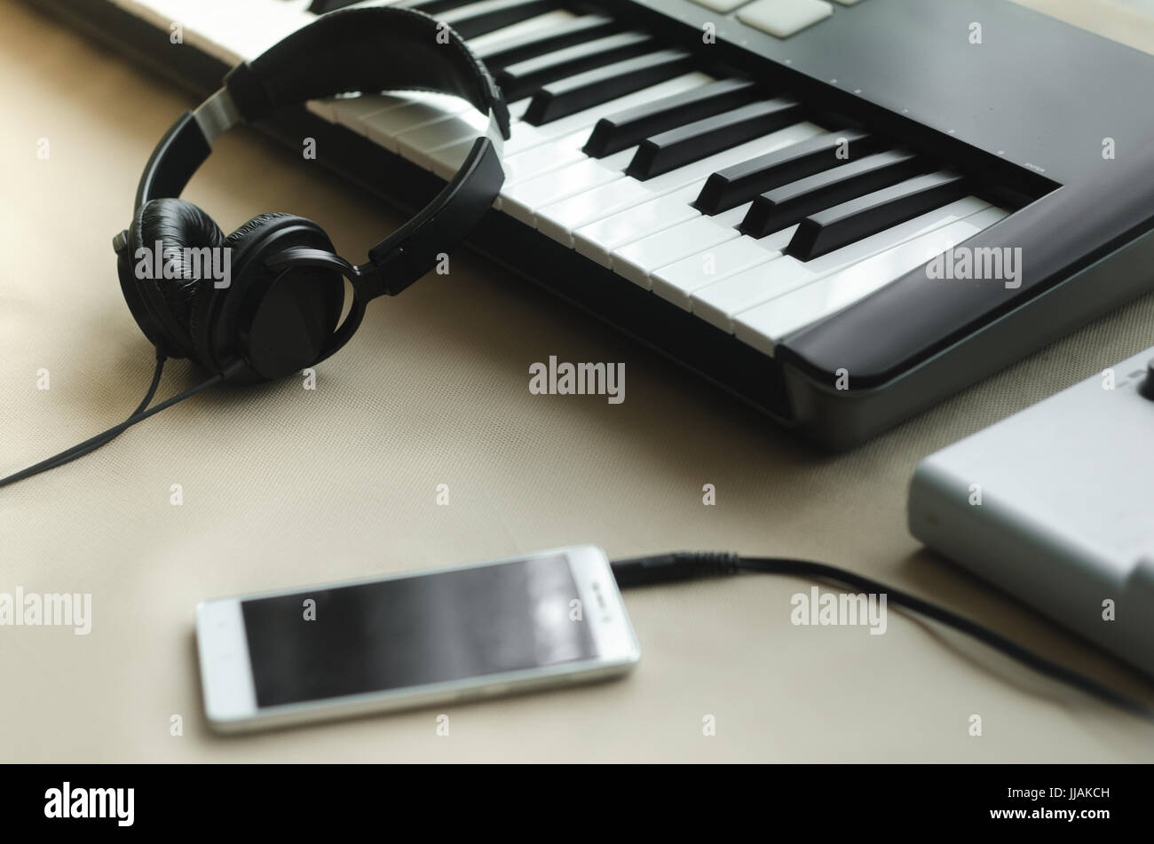 Headphones, synthesizer and a telephone lying on a beige background next to the music console. Side view Stock Photo
