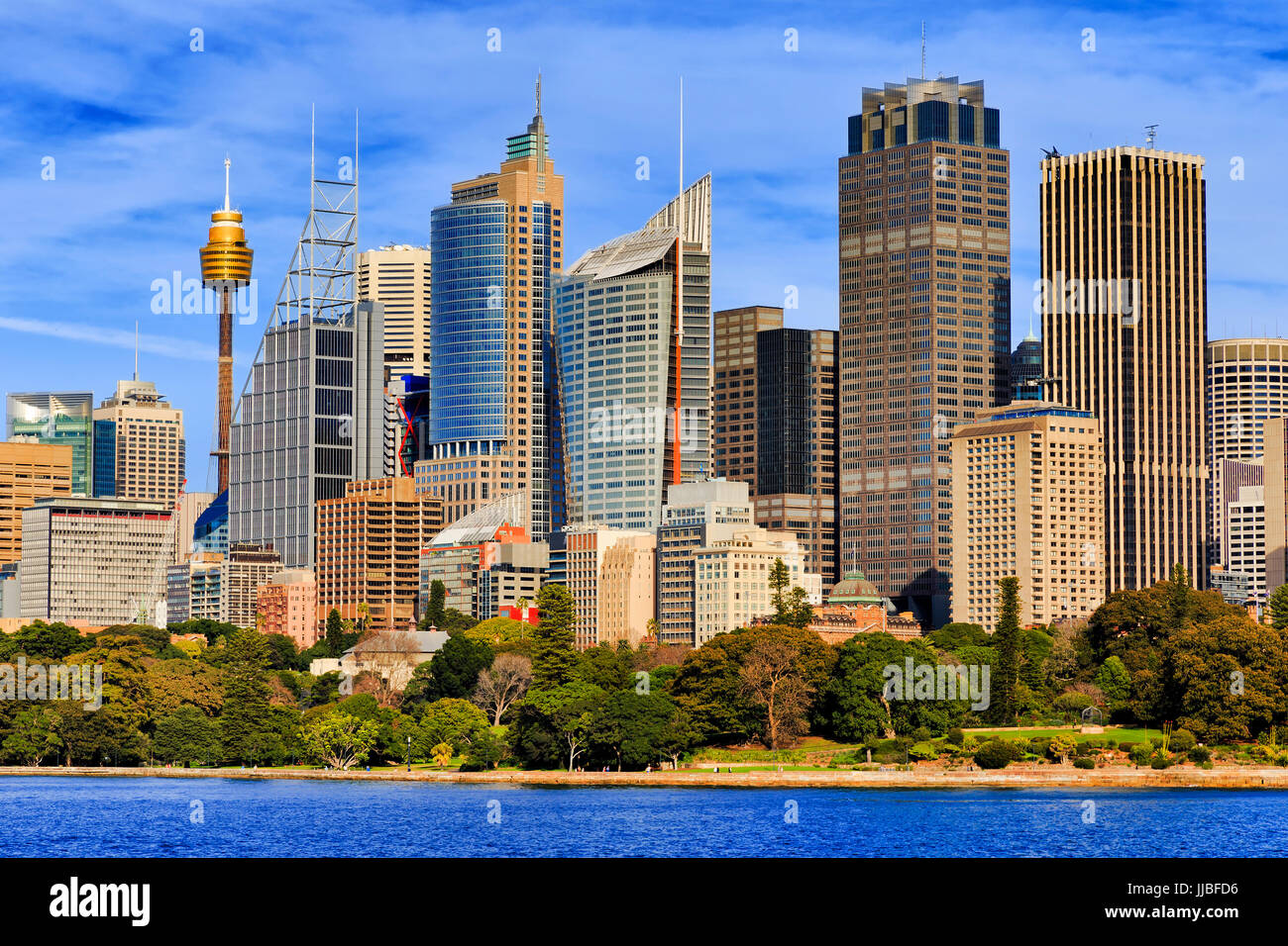 Tall towers of high-rise office buildings in Sydney city CBD standing above the Royal Botanic Gardens as seen from Sydney Harbour on a sunny day. Stock Photo