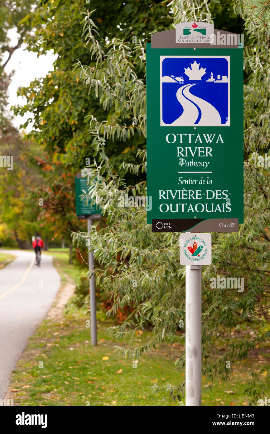A sign for the Ottawa River Pathway or Capital Pathway which is also part of the Trans Canada Trail with a cyclist passing by at Brittania Park. Stock Photo