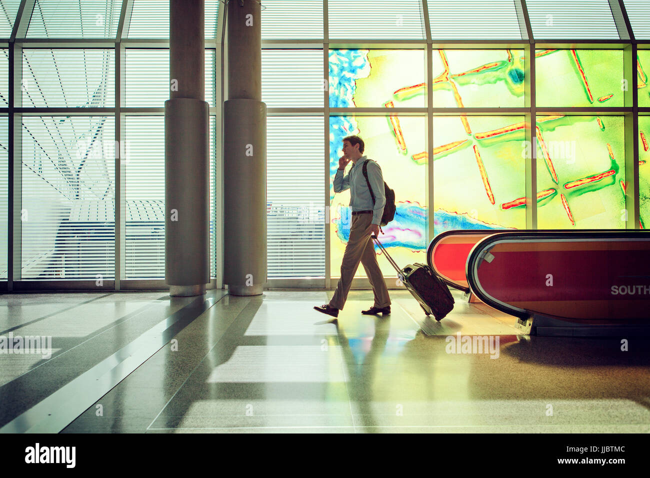 Man talking on cellphone and pulling a bag in an airport. Stock Photo