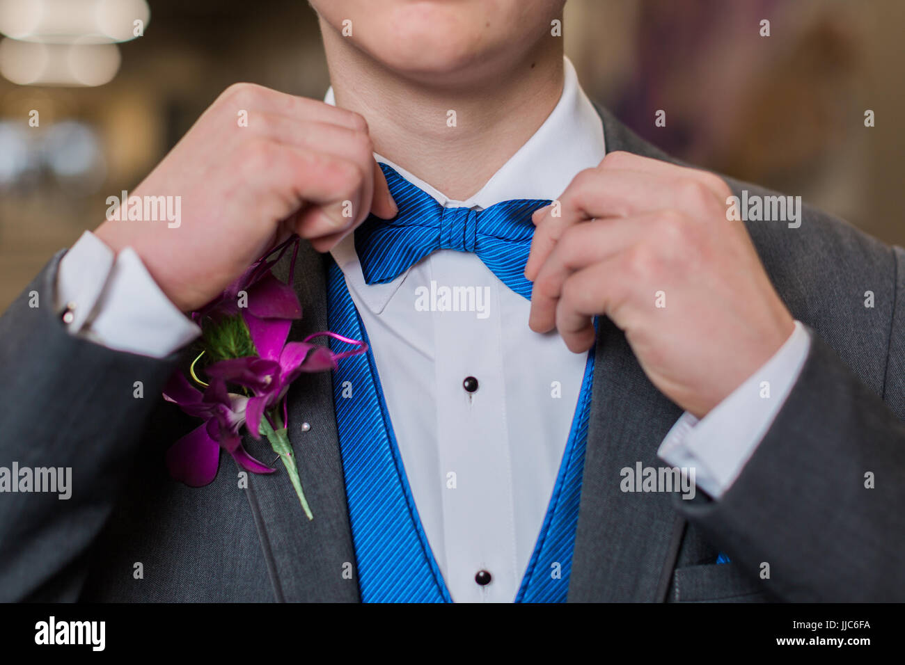 One teen boy adjusts blue striped bow tie. Getting dressed and ready for formal high school prom dance. Stock Photo