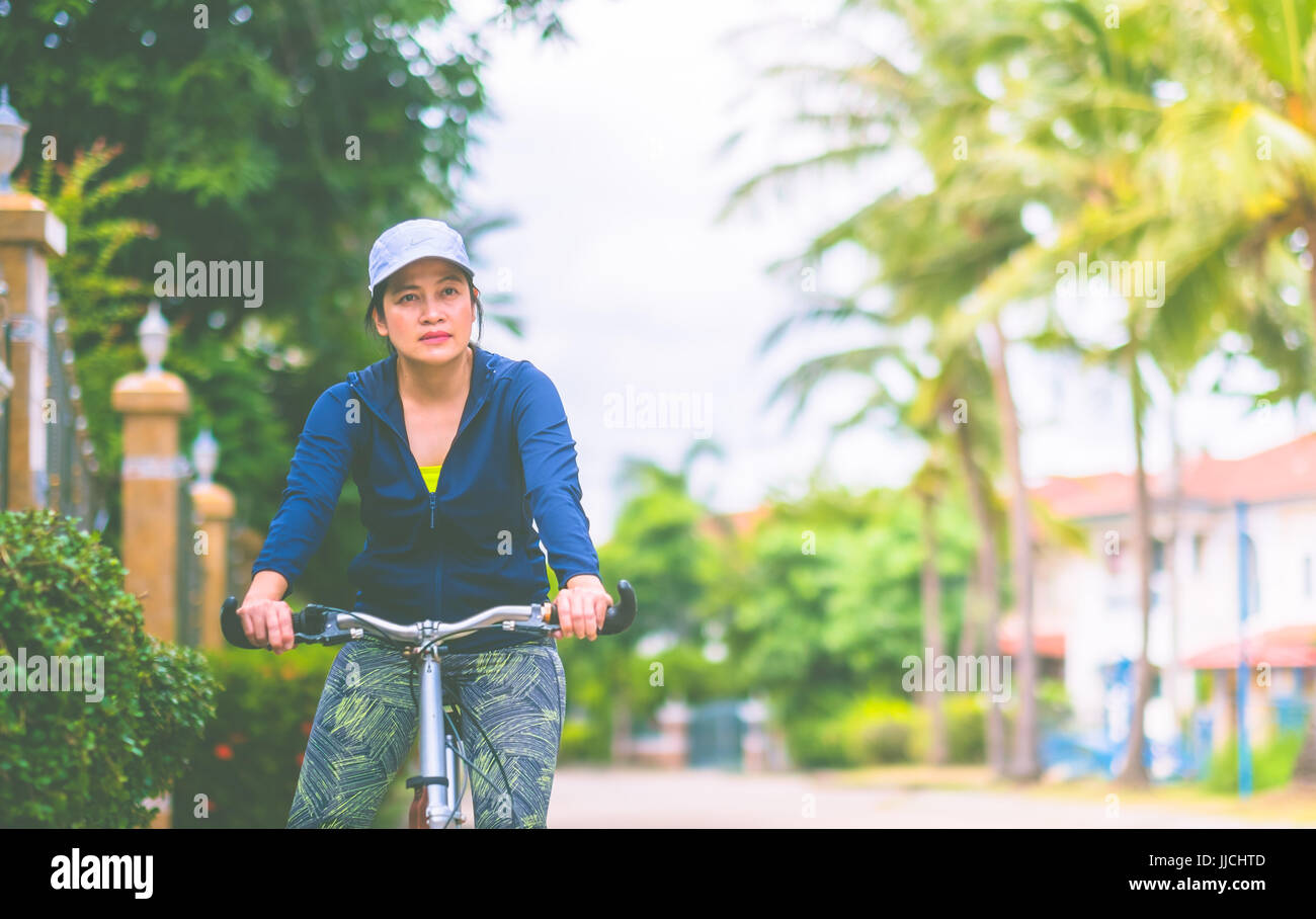 Woman with gym suit ride bike for exercise in village garden in morning time,Healthy lifestyle. Stock Photo