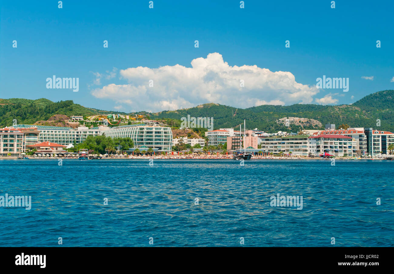 view of beach with hotels, umrellas and sunbeds from sea against blue sky with cloud and water slides at background, Marmaris, Turkey Stock Photo