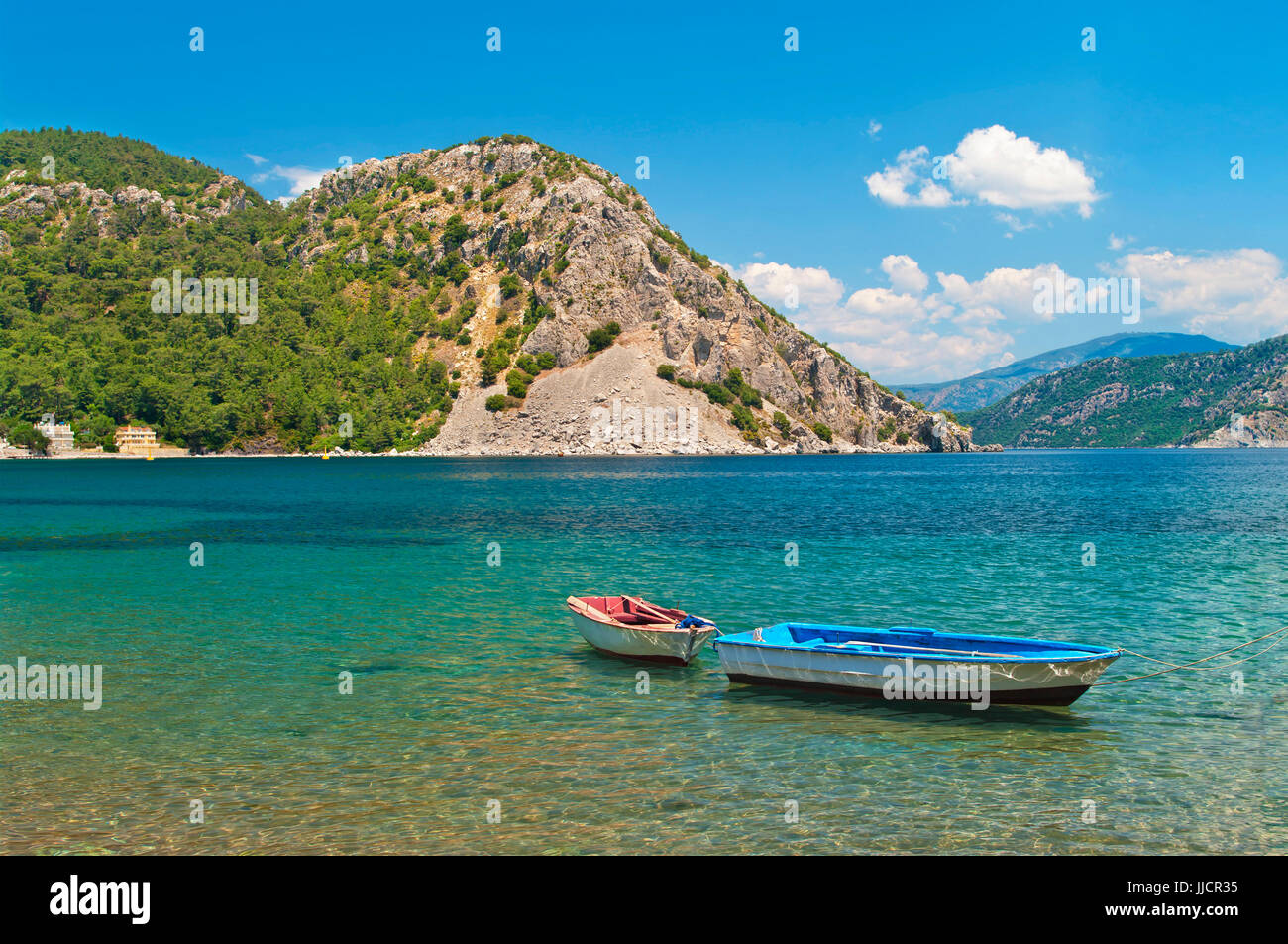 two small boats tied with rope at Aegean sea bay with turquoise waters surrounded by mountains on sunny day, Marmaris, Turkey Stock Photo